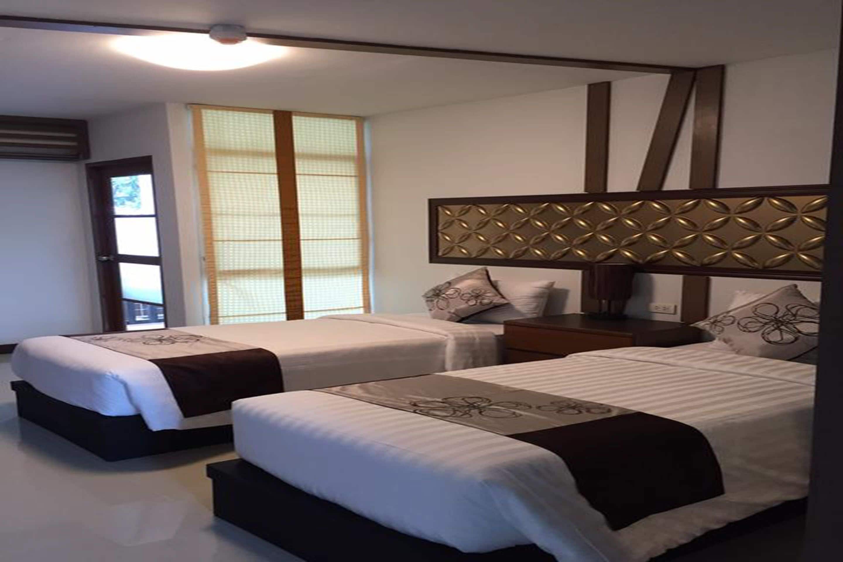 A hotel room with two beds, a wooden headboard, a nightstand, and a window with a view.