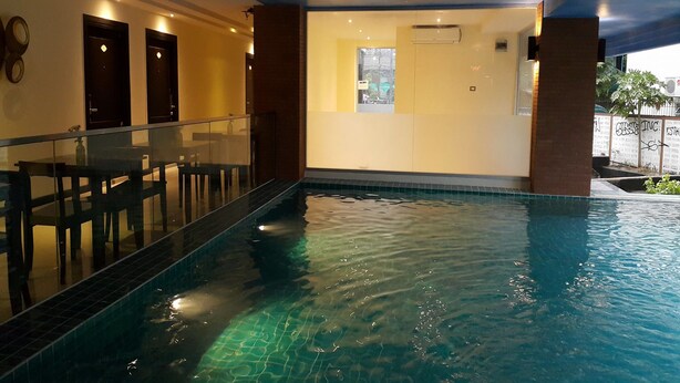An indoor swimming pool with a glass railing, a tiled floor, and a view of the outside through a window. - Leelawadee Modern Resort Huaykwang (Bangkok)