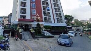 A multi-story hotel with a red and white facade, balconies, and a parking area in front. - Leelawadee Modern Resort Huaykwang (Bangkok)