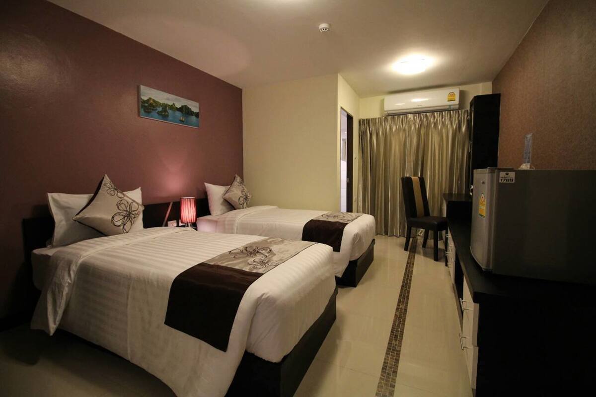 Une chambre d’hôtel avec deux lits, un bureau, une chaise, un réfrigérateur et un tableau au mur.