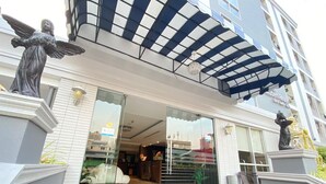 A hotel entrance with a glass facade, a covered entrance area, and a statue of an angel on the left. - Leelawadee Modern Resort Huaykwang (Bangkok)