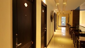 A hotel corridor with dark wooden doors, a glass railing, and a view of the outdoors through a window. - Leelawadee Modern Resort Huaykwang (Bangkok)