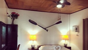 A bedroom with a bed, two wall-mounted lamps, a ceiling fan, a wooden wardrobe, and a vase with flowers on the wall. - Pandan Beach Resort (Pandan)