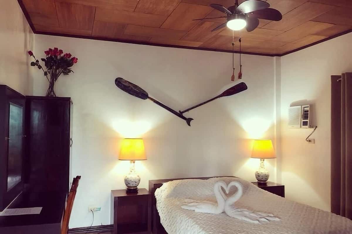 Ein Schlafzimmer mit einem Bett, zwei Wandlampen, einem Deckenventilator, einem Holzschrank und einer Wandvase mit Blumen.