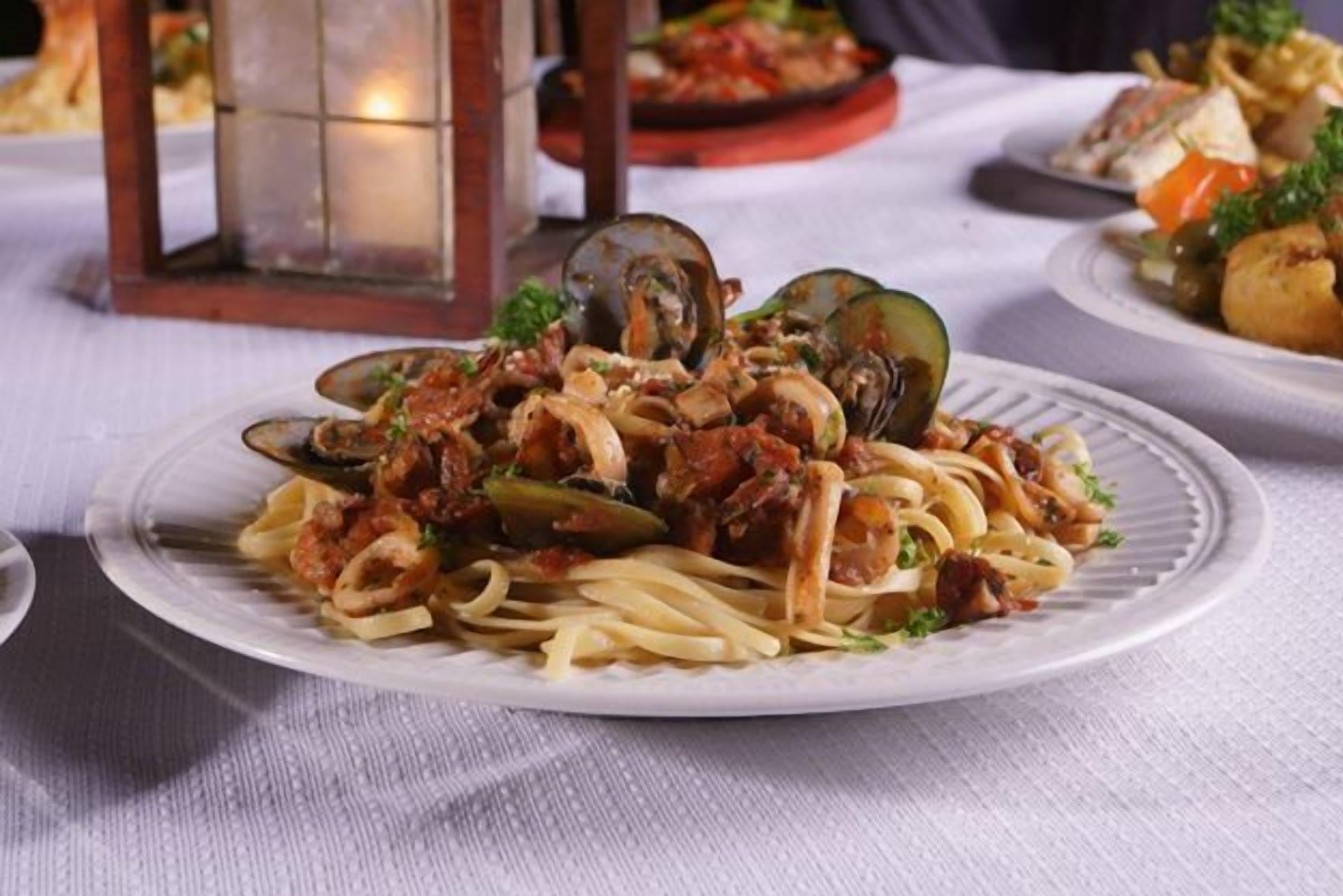 A plate of pasta with clams and vegetables on a white plate.