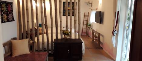 A room with a bed, a small table, a TV mounted on the wall, and a sliding door leading to another area.