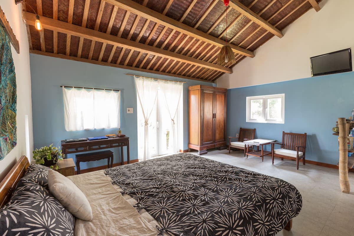 Un dormitorio con cama, escritorio, sillas, techo de madera y televisor en la pared.