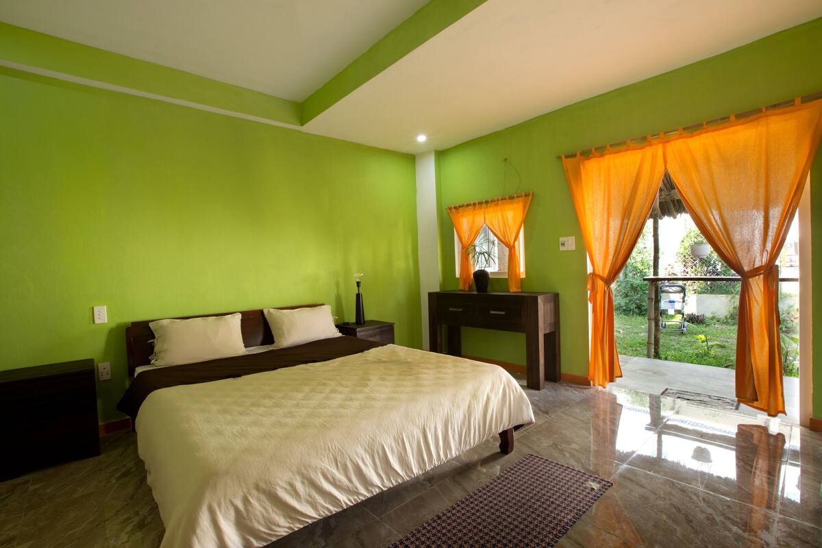Un dormitorio con cama, mesitas de noche, cómoda y ventana con cortinas naranjas.