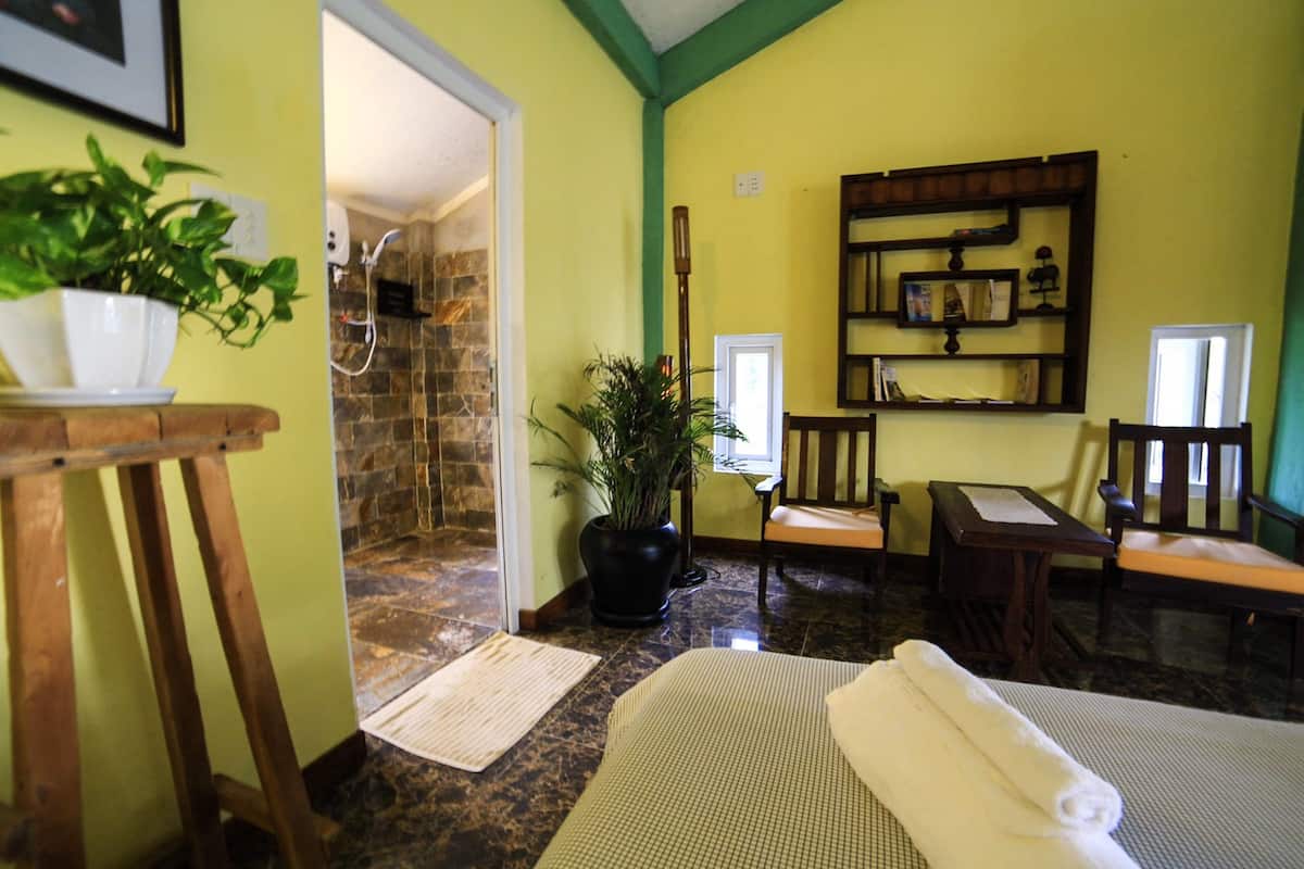 Una habitación con ducha de piedra, una planta en maceta, una mesa de madera, un banco y una estantería.