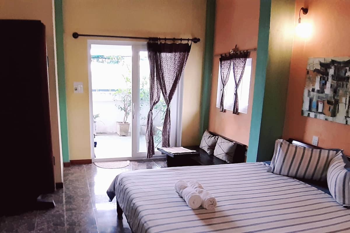 Habitación de hotel con cama, una mesita y una silla. Se ve una ventana con cortinas y vistas al exterior.