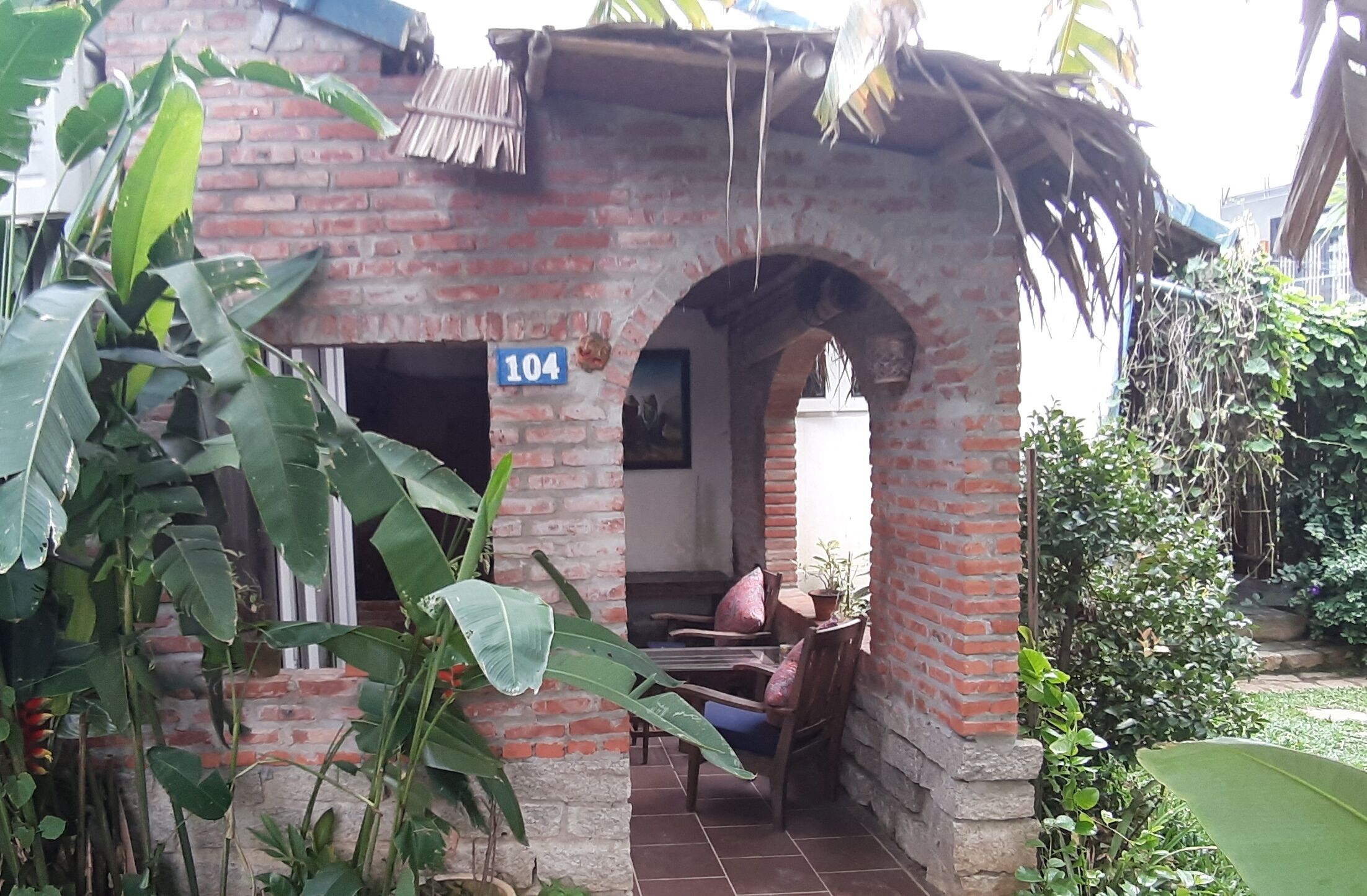A brick building with a number '104' sign, a covered porch, and a chair.