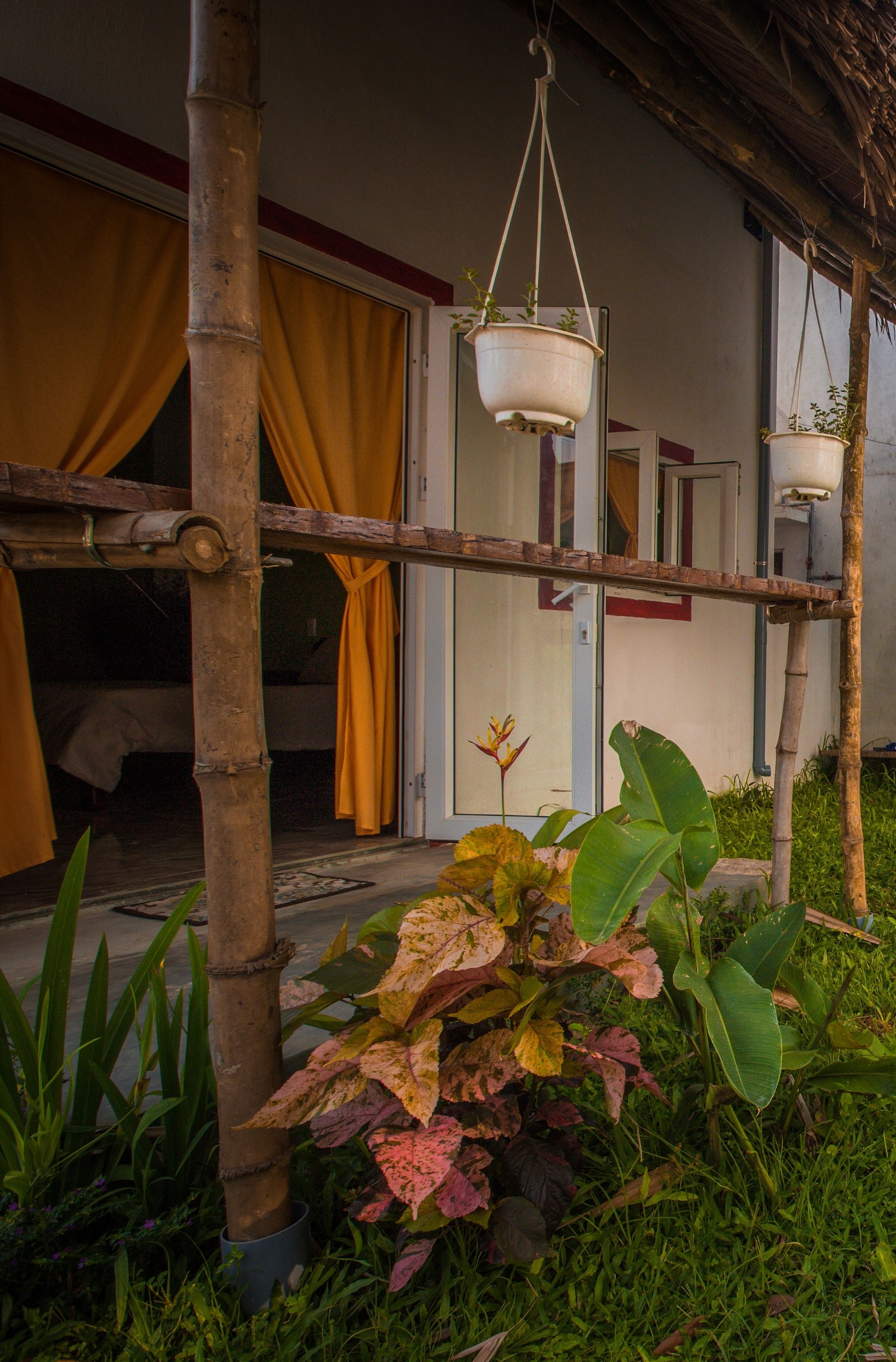A bamboo structure with hanging planters, a bed with yellow curtains, and a door with a red frame.