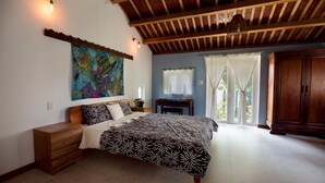 Une chambre à coucher avec un lit, une commode en bois, un tableau au mur et une vue par la fenêtre.