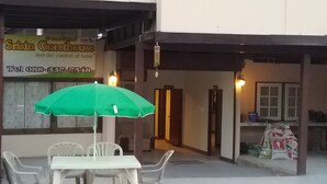 Una mesa con sombrilla verde, sillas blancas y mantel blanco frente a un edificio con un cartel que dice 'Strisin Guesthouse'.