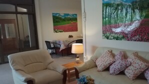 Una sala de estar con un sofá color beige, una mesa de centro de madera y una silla. En la pared hay un cuadro de un paisaje y una lámpara sobre la mesa.