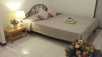 A neatly made bed with floral pillows, a bedside table with a lamp and a flower vase, and a bouquet of flowers on the floor.