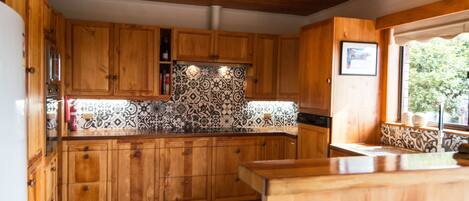 A kitchen with wooden cabinets, a patterned backsplash, and a window with a view of greenery.