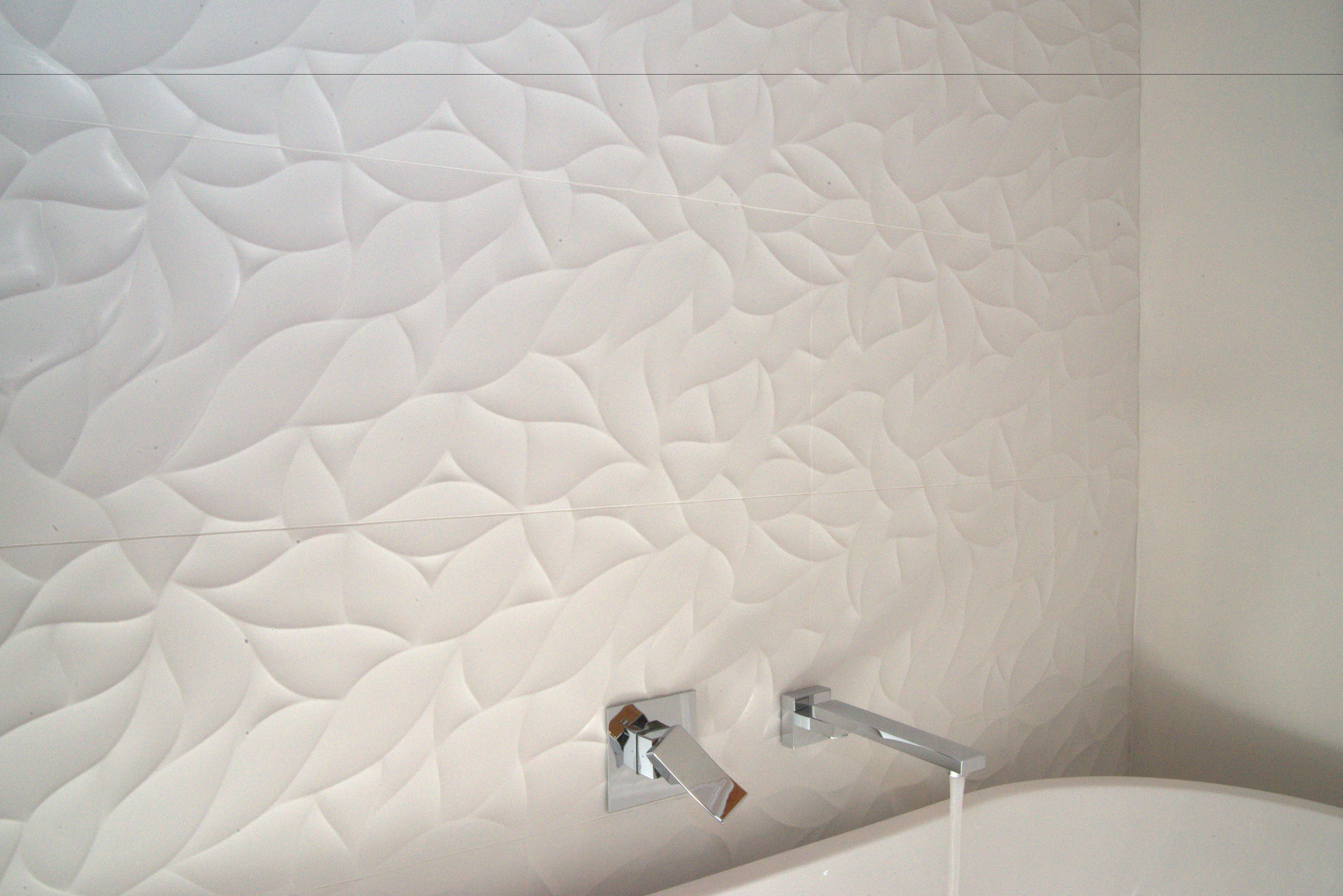 A bathroom with a textured white wall and a modern chrome faucet.