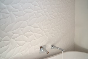 A bathroom with a textured white wall and a modern chrome faucet. - The Hobart Entrance (Kingston)