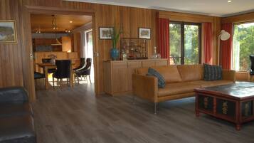 A spacious living room with a wooden floor, a leather sofa, a coffee table, and a dining area with a wooden table and chairs.