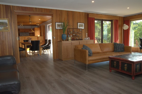 A spacious living room with a wooden floor, a leather sofa, a coffee table, and a dining area with a wooden table and chairs. - The Hobart Entrance (Kingston)