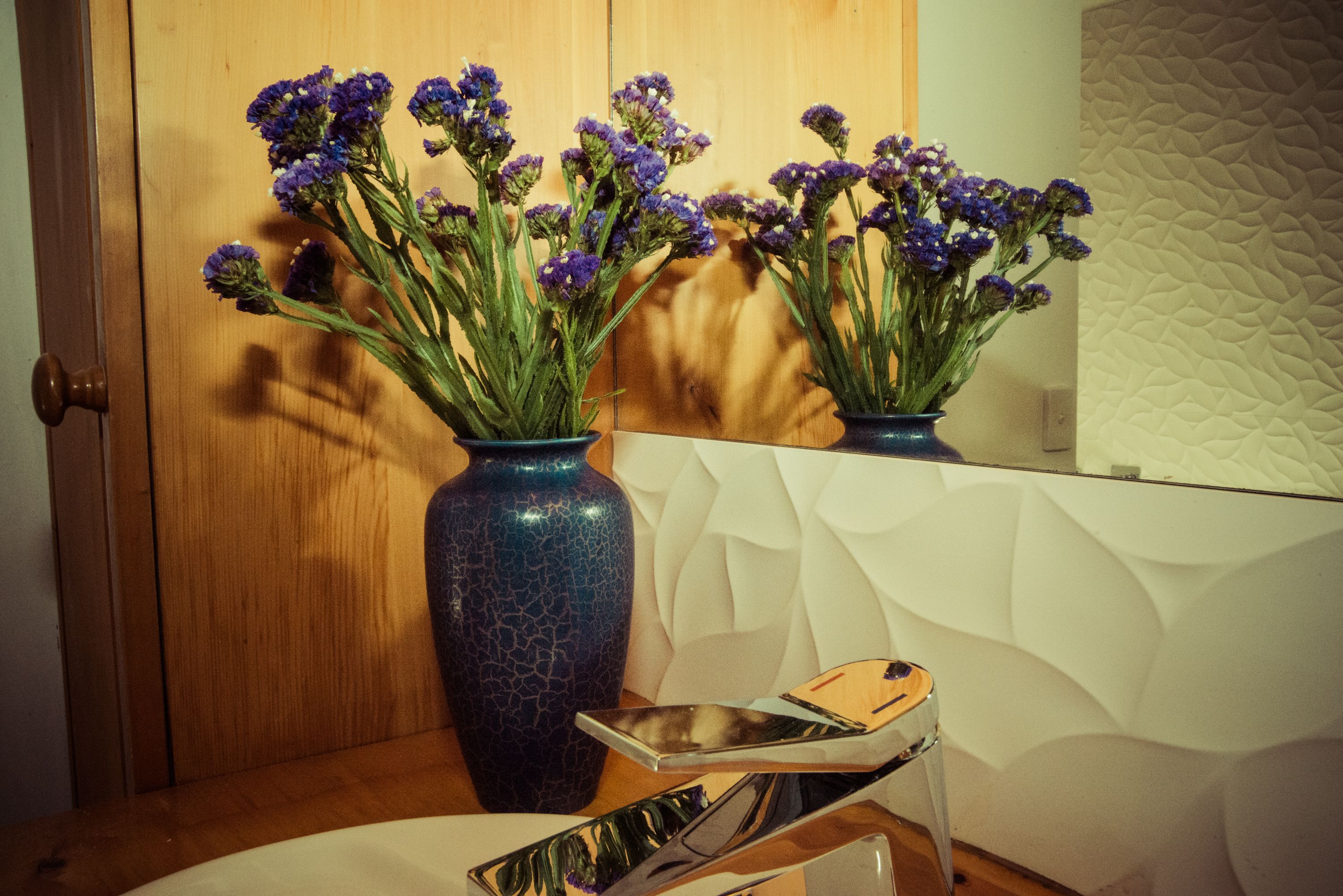 A wooden door with a mirror reflecting a vase with purple flowers.