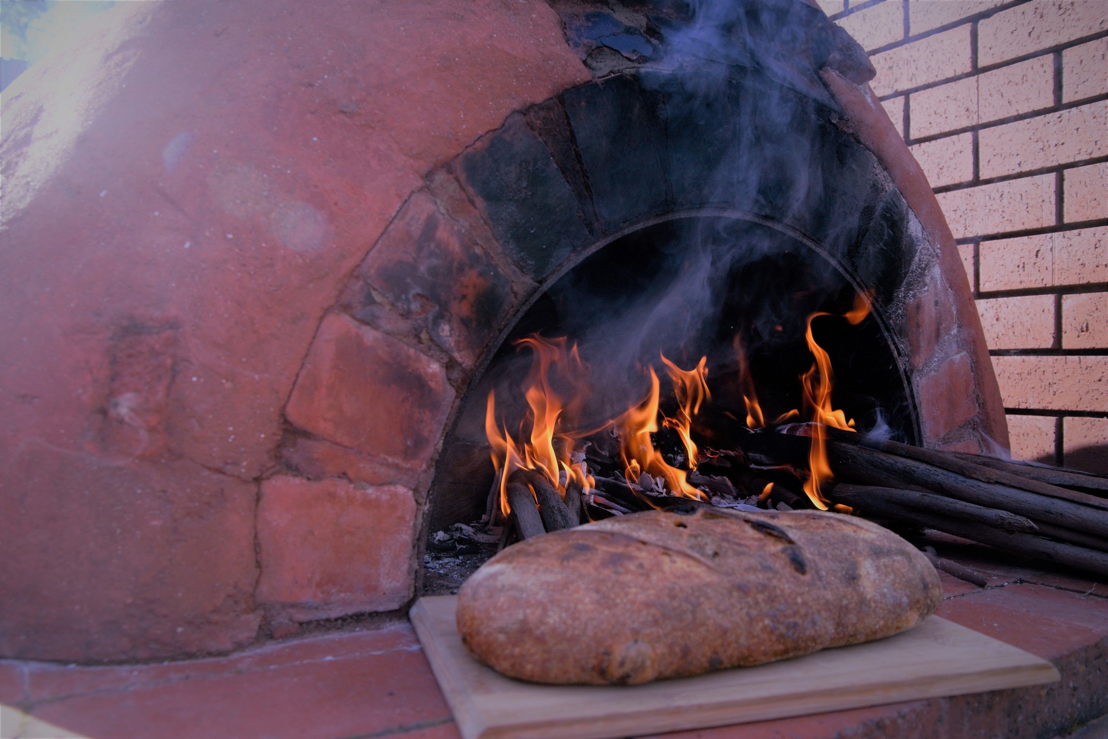 A brick oven with flames and a loaf of bread on a cutting board.