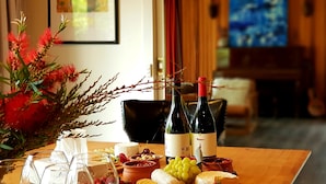 A dining table with wine bottles, cheese, grapes, and a vase of red flowers. - The Hobart Entrance (Kingston)