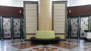 Eine Lobby mit einem Schachbrettmuster auf dem Boden, einer zentralen Säule und einer Sitzecke mit grünen Kissen.