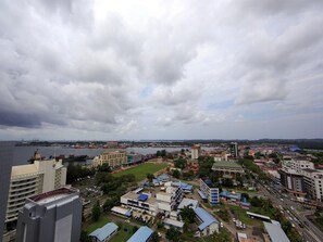 A cityscape with a mix of commercial and residential buildings, a large body of water in the background, and a cloudy sky.