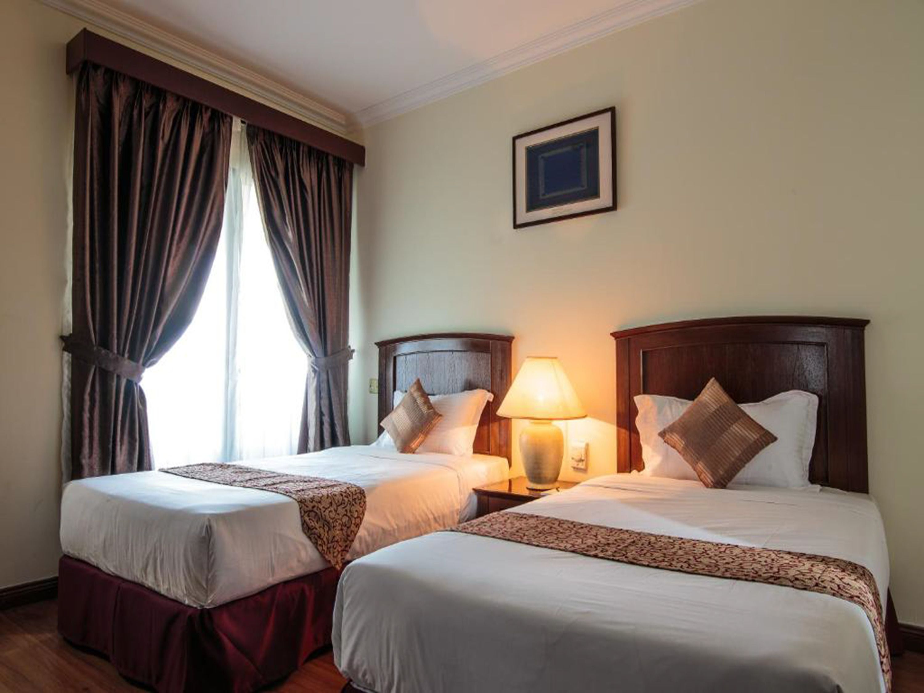 A hotel room with two beds, a nightstand with a lamp, and a window with curtains.