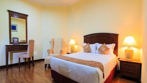Ein Hotelzimmer mit einem großen Bett, zwei Nachttischen mit Lampen, einem Schreibtisch mit Stuhl und einem Spiegel an der Wand.