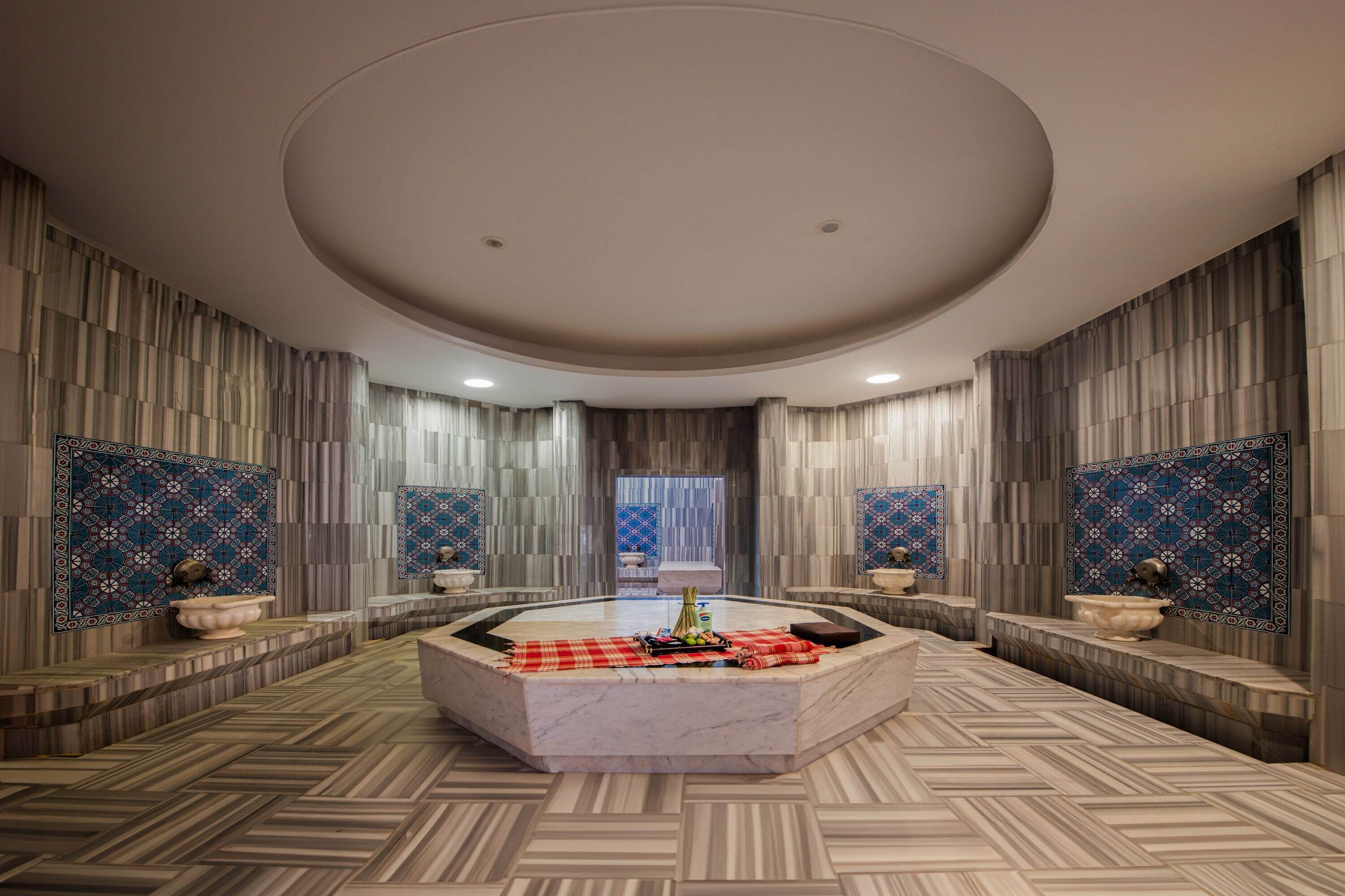 A spacious bathroom with a central marble sink, decorative tiles, and a unique ceiling design.