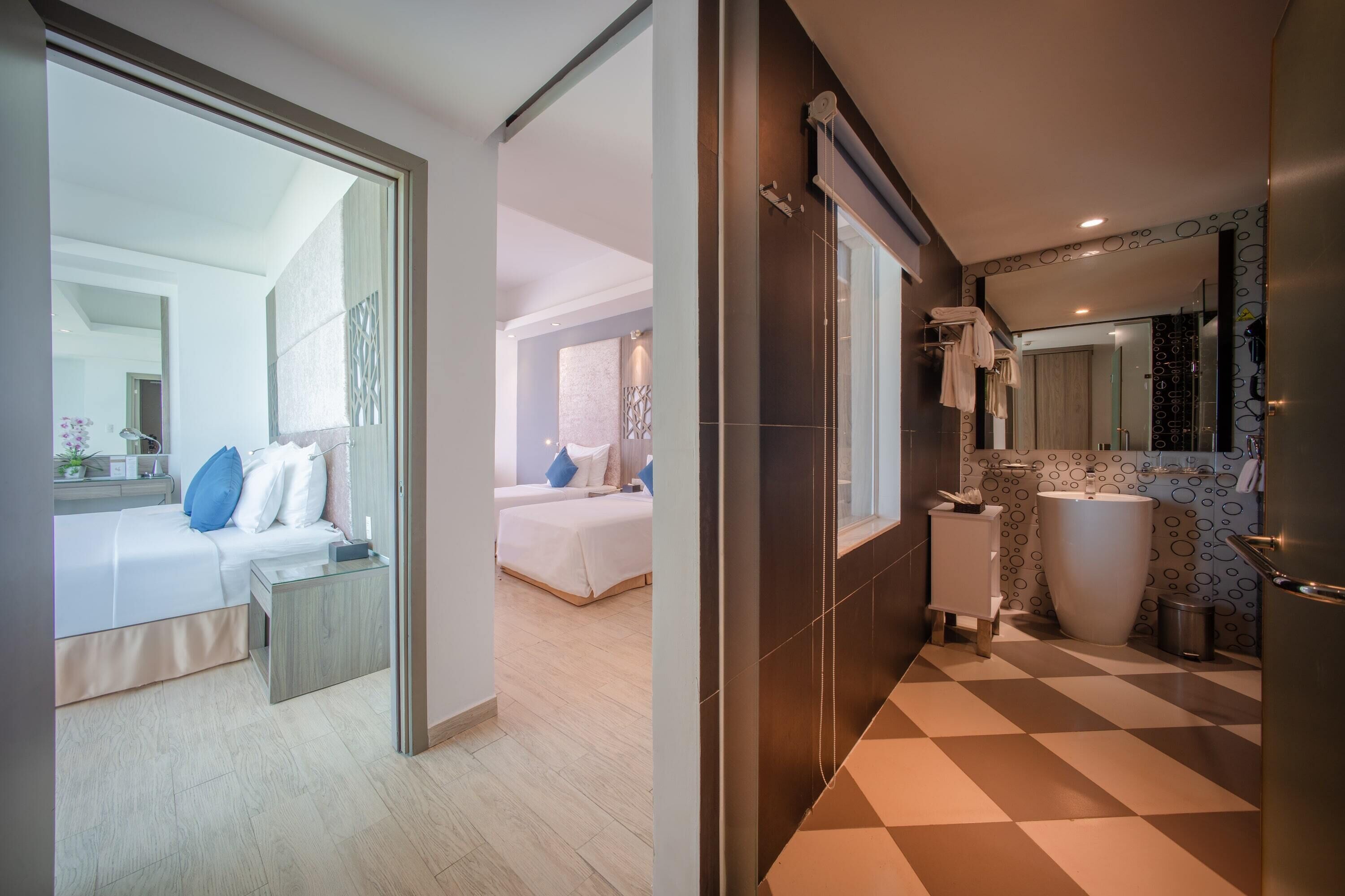 A modern hotel room with a large bed, a separate bathroom with a large mirror, and a checkered floor.