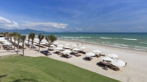 Une plage avec des parasols blancs, des chaises longues et des palmiers.