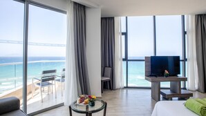 Une chambre d’hôtel avec un balcon, une télévision, un lit et une petite table sur laquelle se trouve un panier de fruits.