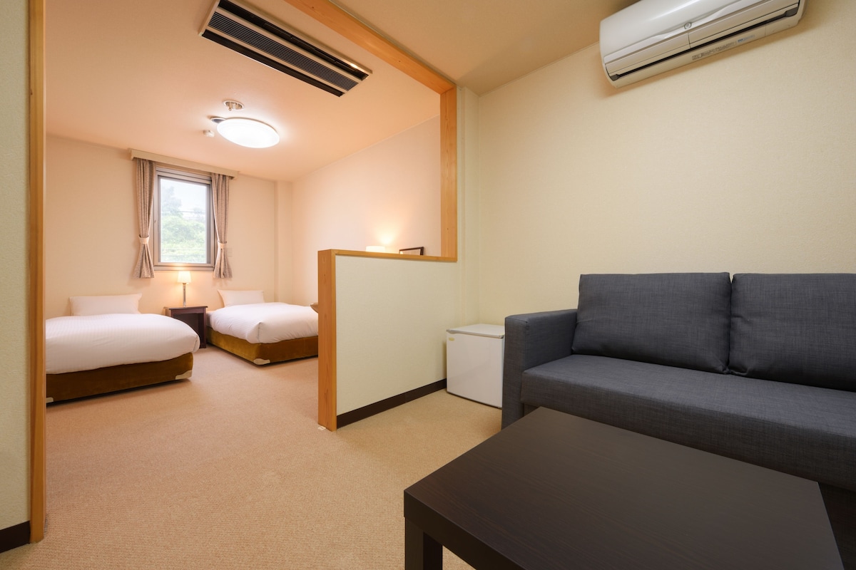 Une chambre d’hôtel avec deux lits, un canapé, une petite table et un bureau.