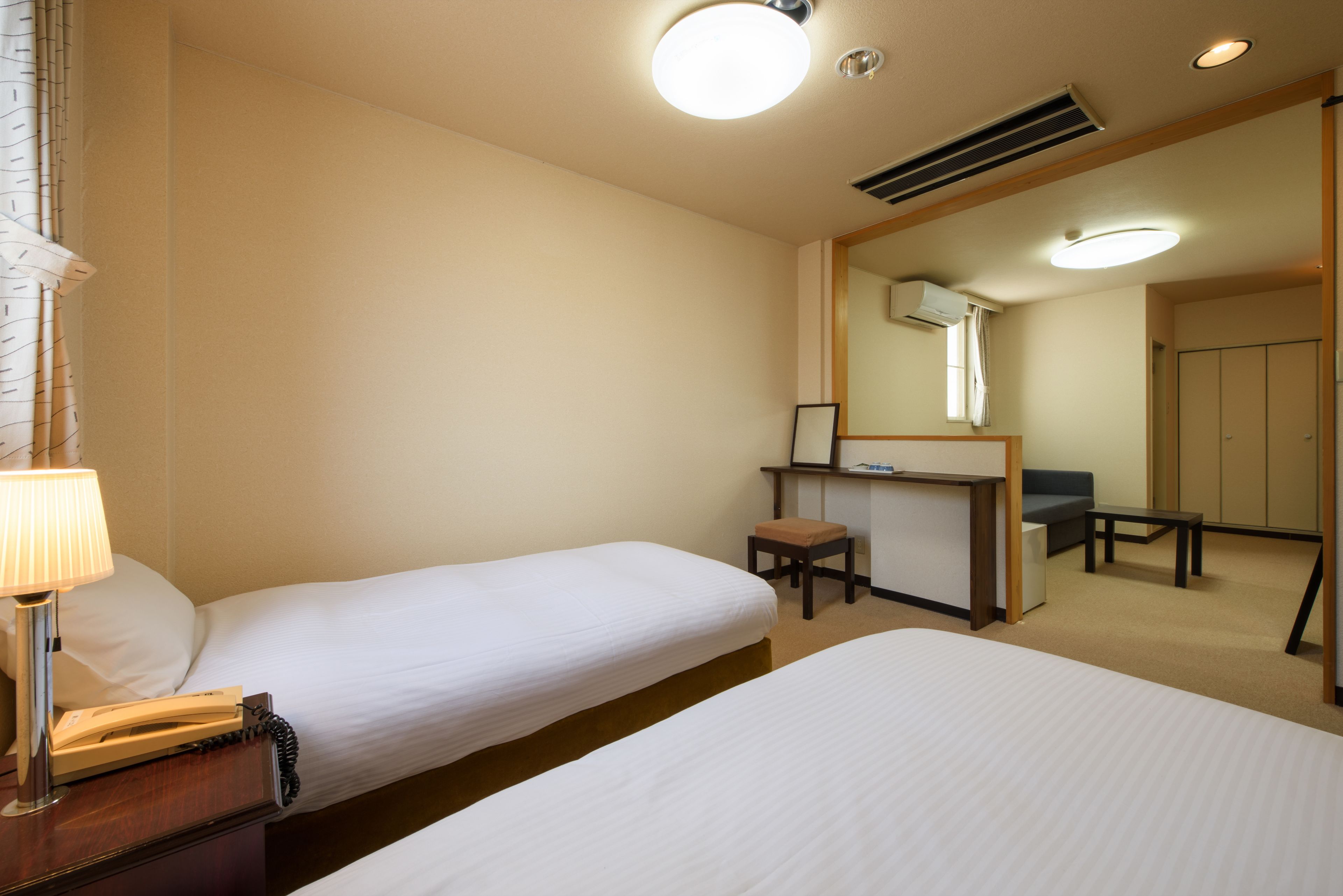 A hotel room with two single beds, a desk with a chair, a mirror, and a small table.
