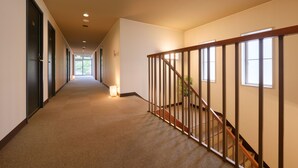 Un pasillo largo y estrecho con pisos alfombrados, barandales de madera y una escalera a la derecha.