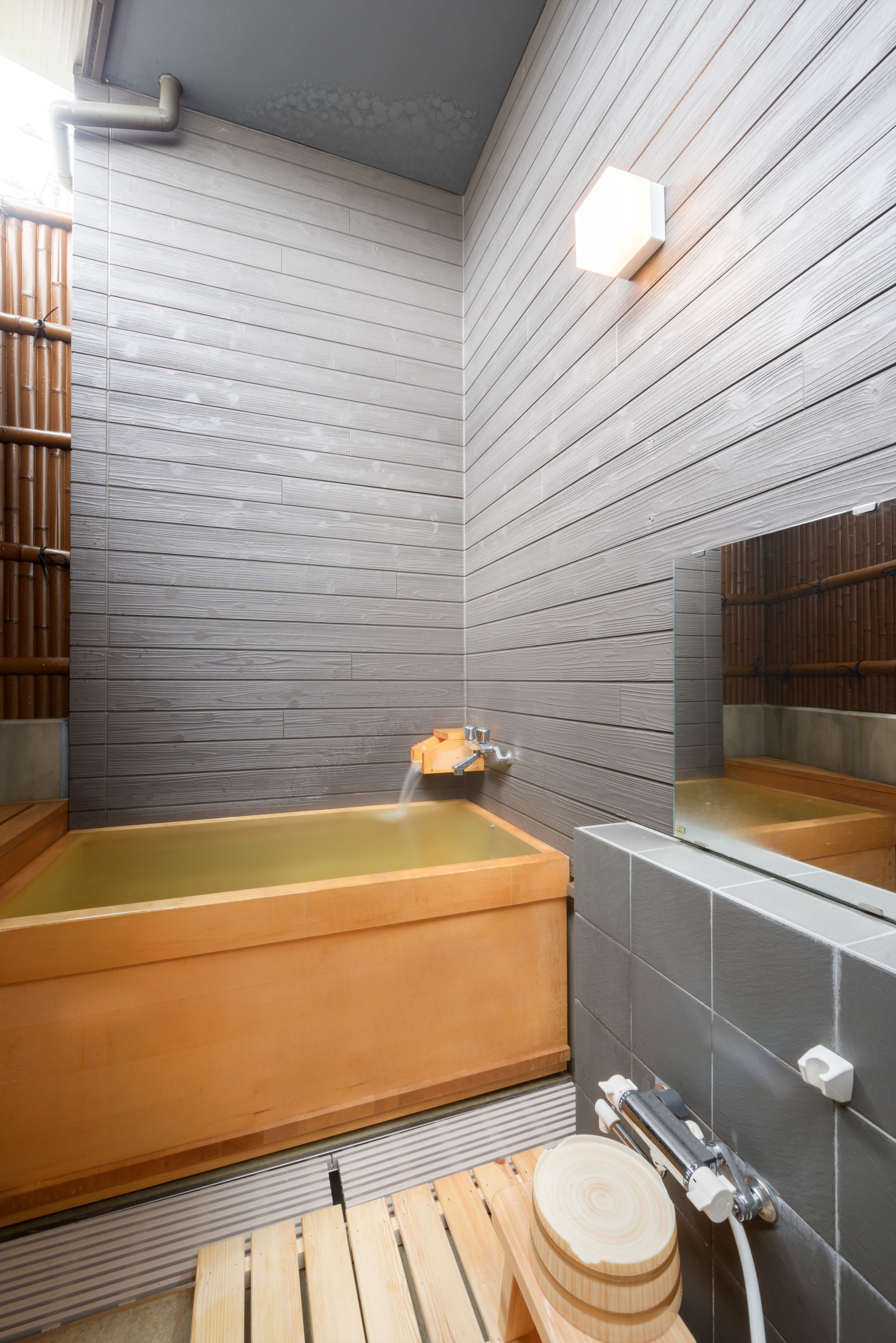 Een traditioneel Japans bad met een houten badkuip, een houten zitje en een betegelde muur.