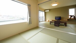 Una habitación con suelo de tatami, televisión, escritorio y ventana con cortinas.