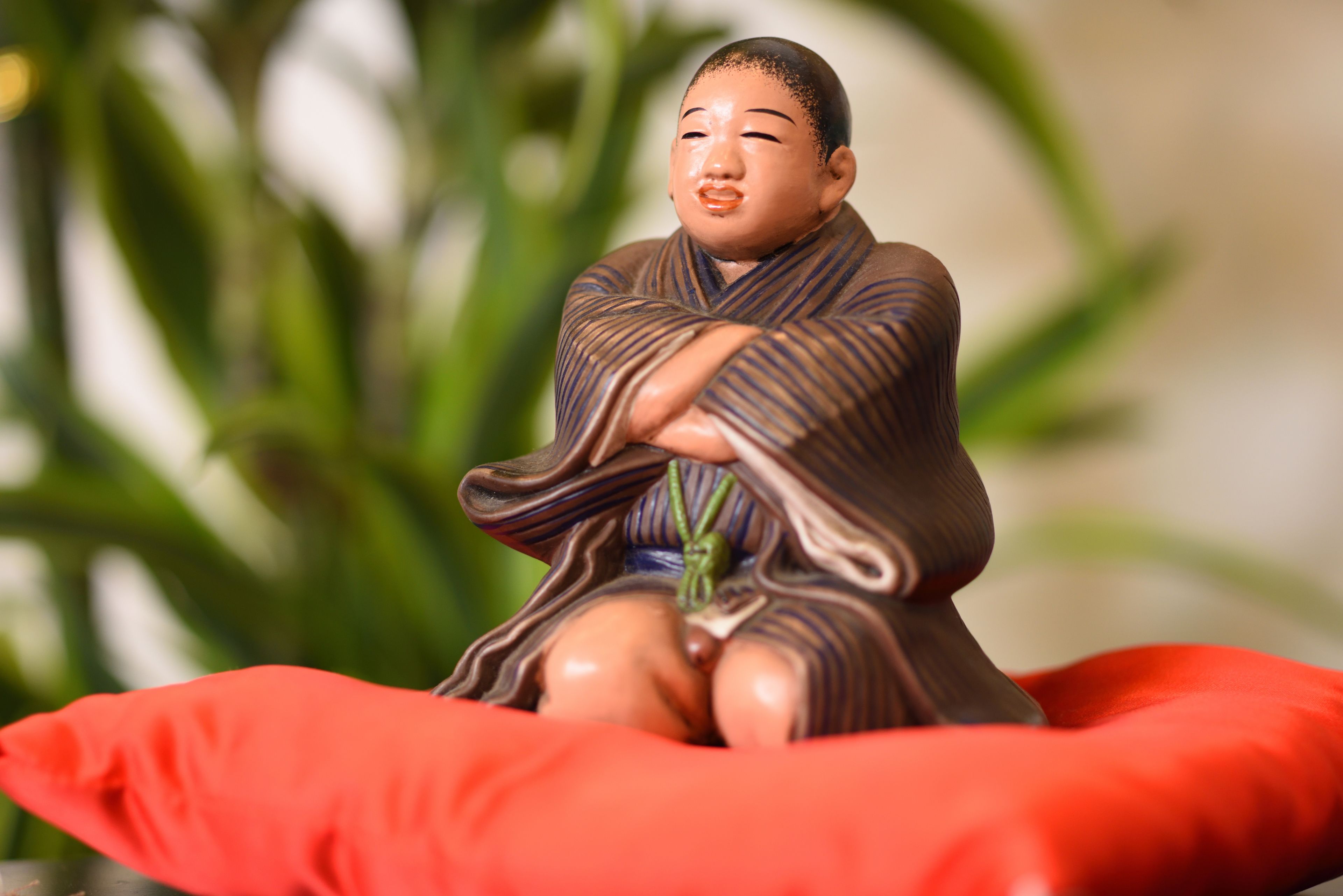 A statue of a seated figure in traditional attire on a red cushion.