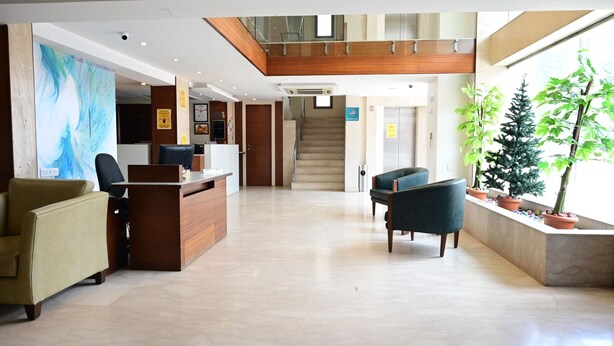A spacious lobby with a reception desk, seating area, staircase, and potted plants. - The Horizon Comforts (Bengaluru)