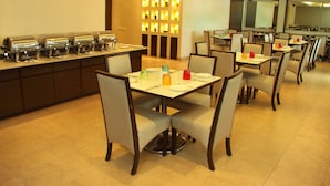 A hotel dining area with multiple tables and chairs, a buffet line with food dispensers, and a wall of illuminated lights. - The Horizon Comforts (Bengaluru)