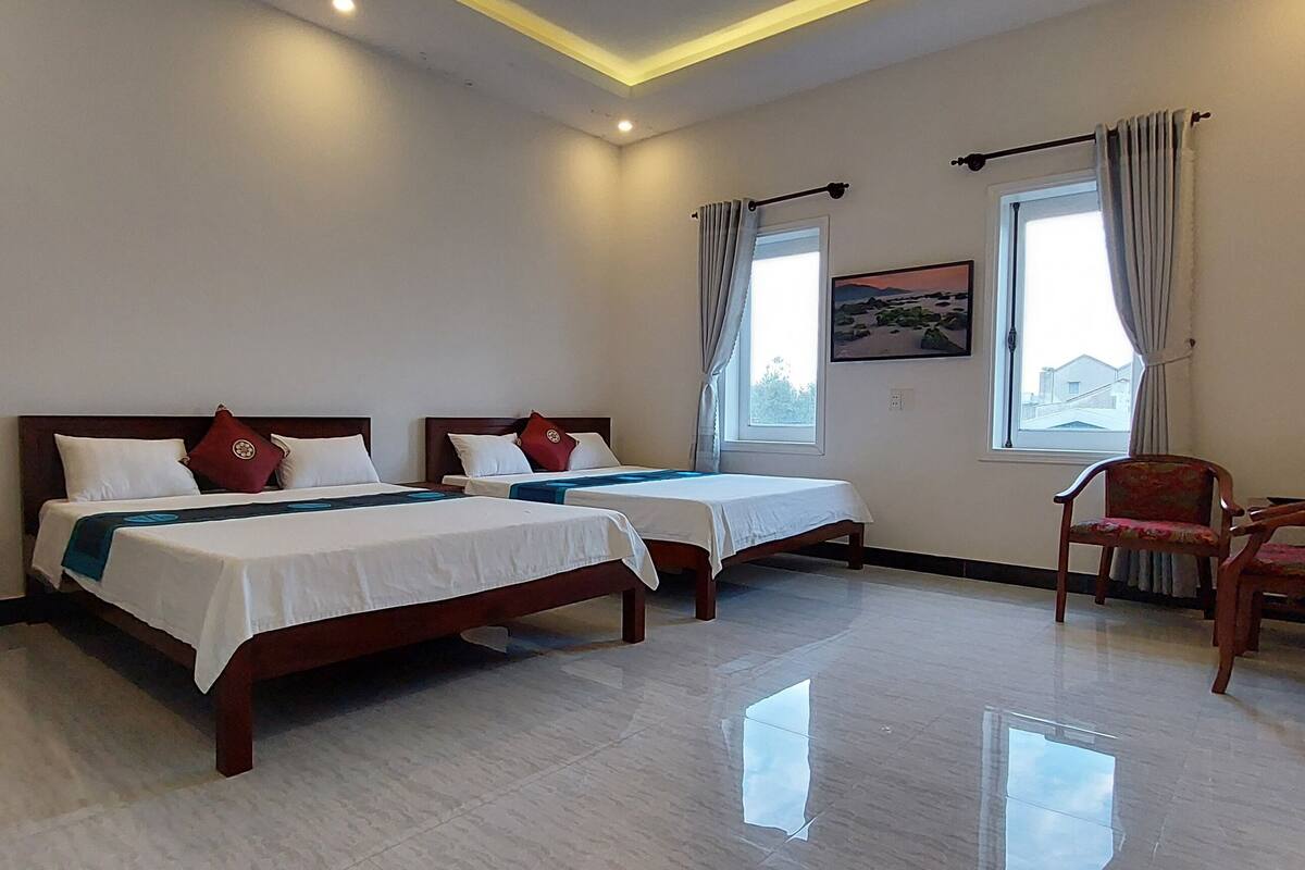 A hotel room with two beds, a chair, and a window with curtains.