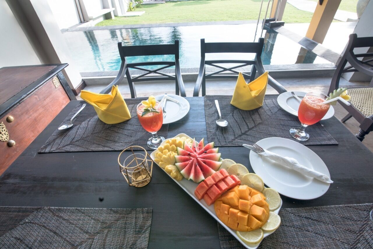 A table set with a fruit platter, two drinks, and a glass of water, overlooking a pool.