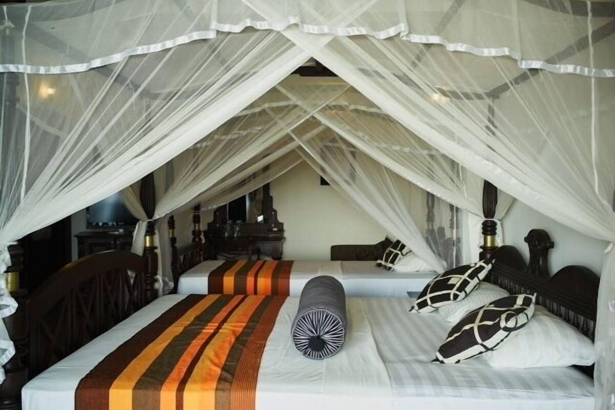A room with a bed under a mosquito net, two bedside tables, and a nightstand.