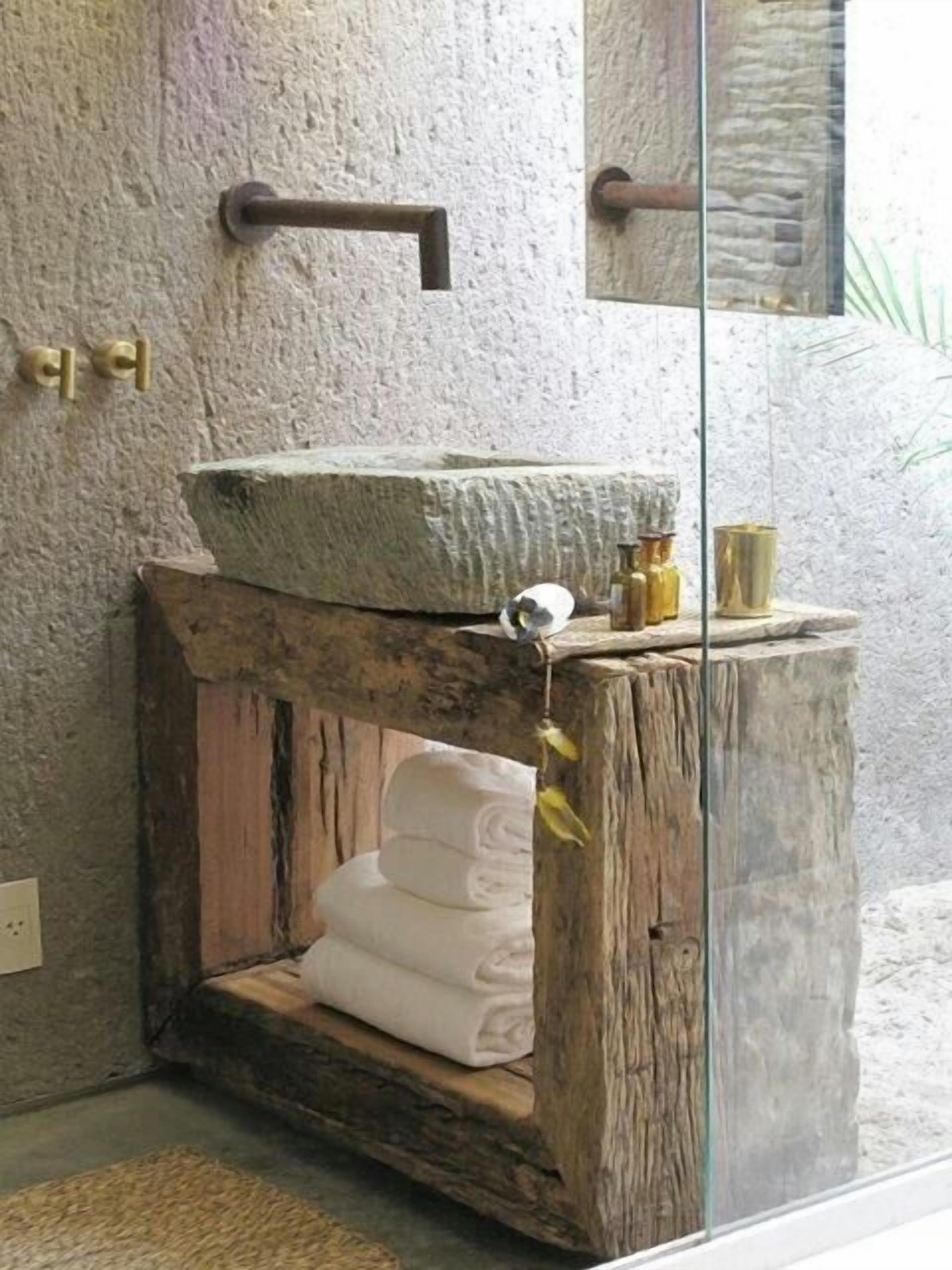 A rustic bathroom with a stone sink, wooden vanity, and a mirror.