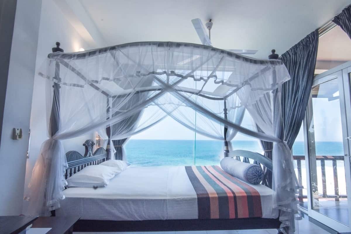 A bed with a canopy, a view of the sea, and a balcony with curtains.