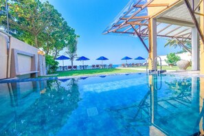 A clear swimming pool with lounge chairs and umbrellas, surrounded by greenery and a clear sky. - Amanda Beach Villas (Unawatuna)